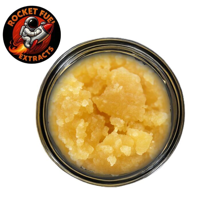 Golden-yellow cannabis concentrate in a clear glass jar on a white background, showcasing its grainy, crystalline texture and rich color
