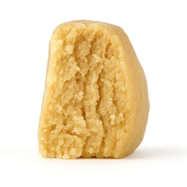 close-up of a light beige, crumbly concentrate piece displayed on a crisp white background, showing fine granular texture and natural depth with soft, even lighting.