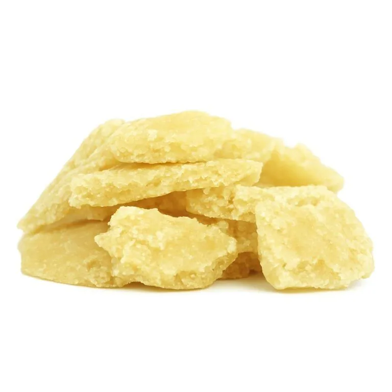 High-resolution close-up of pale yellow cannabis crumble stacked on a crisp white background, showcasing its flaky, crystalline texture and natural matte finish.