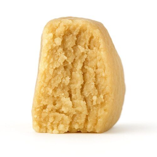 close-up of a light beige, crumbly concentrate piece displayed on a crisp white background, showing fine granular texture and natural depth with soft, even lighting.