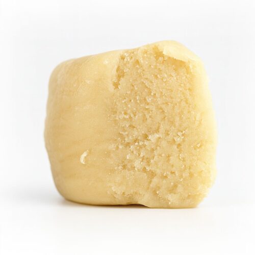 Close-up of a pale beige cube of cannabis extract on a crisp white background, showcasing a fine crumbly texture with subtle lighting and realistic surface detail.