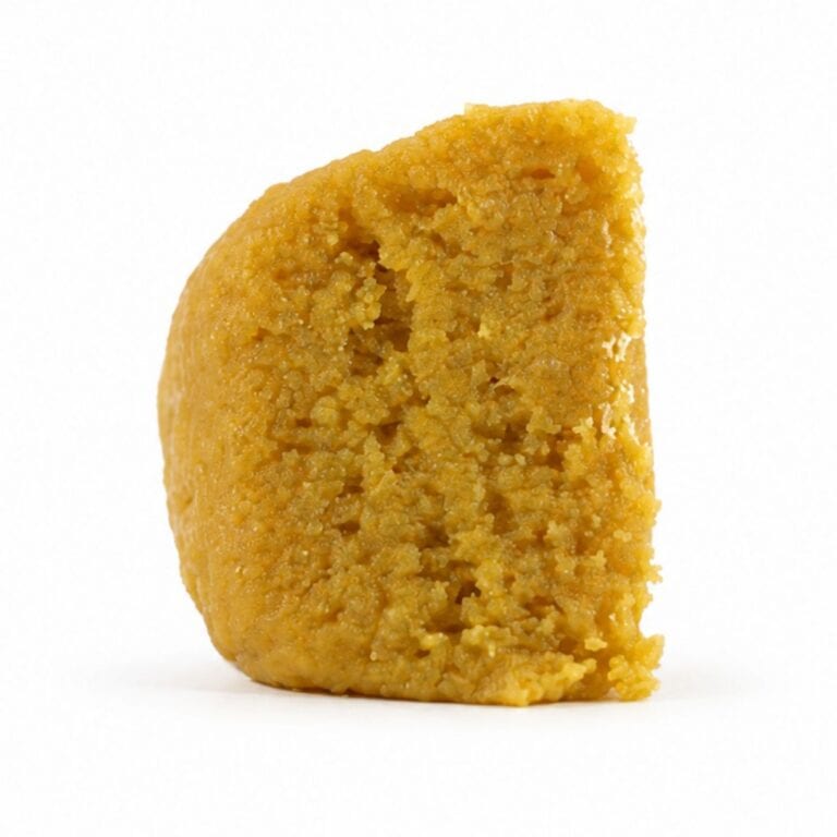 mai tai budder Close-up Pale yellow cannabis extract with a crumbly texture displayed upright on a white background