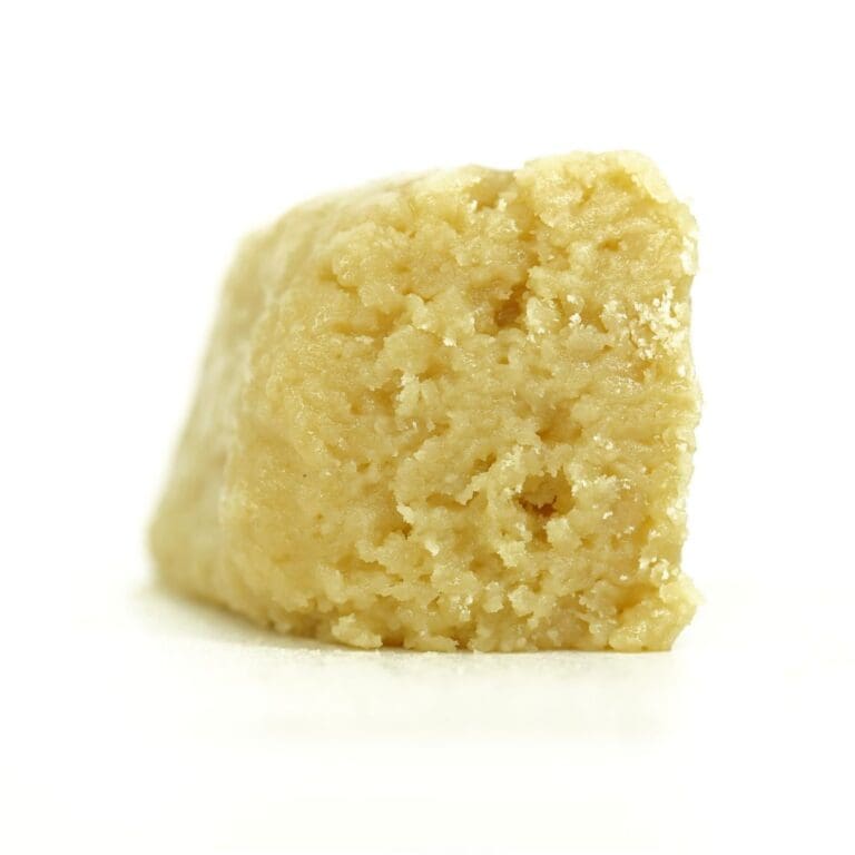 Pale yellow cannabis extract with a crumbly texture displayed upright on a white background