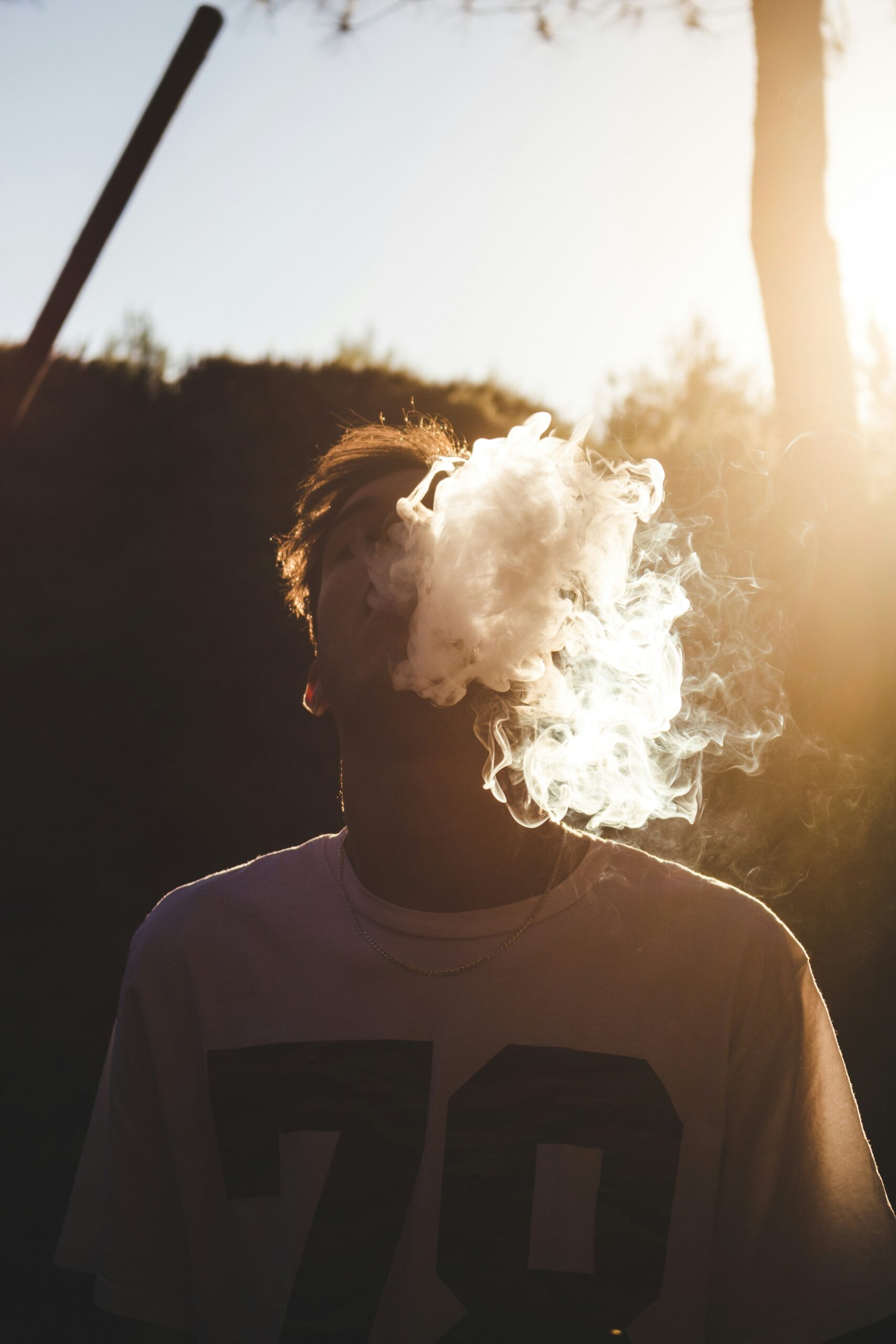 A young man exhales a thick cloud of smoke outdoors at sunset. Image by Daniel Ramos on Unsplash.com.