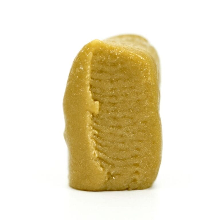 Close-up of a golden-brown cannabis concentrate piece with smooth texture and ridged details on a white background